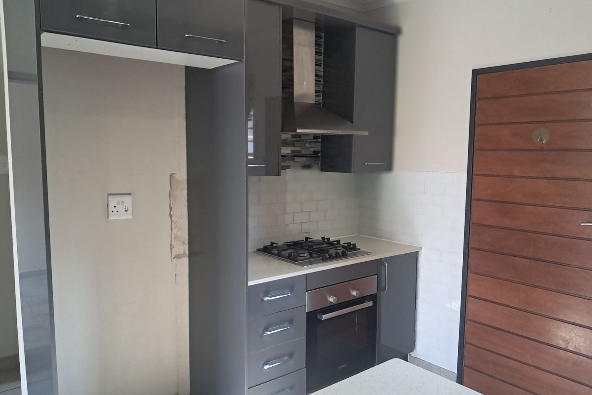 Modern kitchen featuring dark grey cabinetry, built-in oven, gas hob, and subway tile backsplash, requiring minor wall finishing near the fridge space.