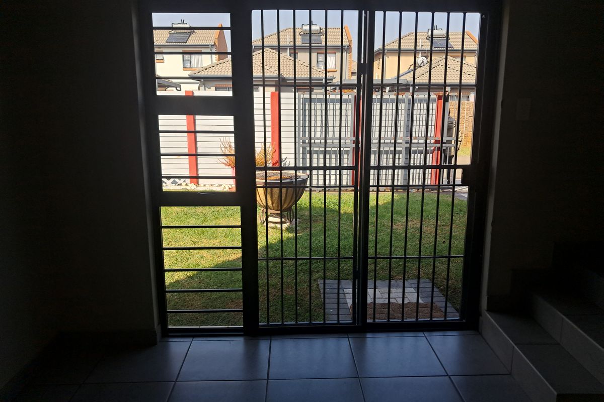 Interior view looking out through a security gate and sliding door towards a private garden area.