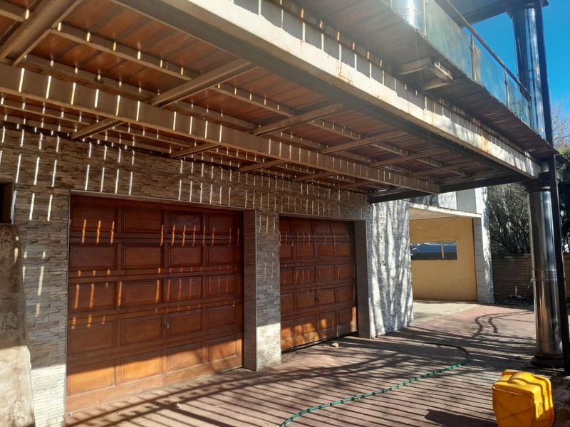 A double garage featuring timber doors, stone cladding, and a covered timber ceiling structure with steel support beams.