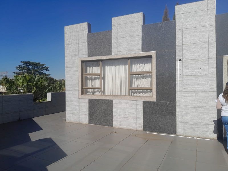 A spacious outdoor patio area featuring modern stone-clad exterior walls and tiled flooring, providing a clean and contemporary outdoor living space.
