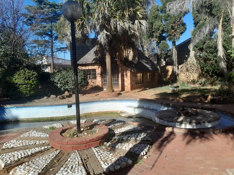 Outdoor pool area featuring a swimming pool, brick paving, and a detached thatched-roof outbuilding set within a mature garden.
