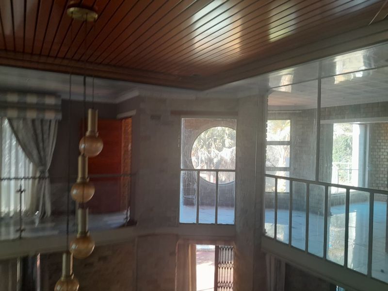 Spacious living area featuring a timber ceiling, large windows with circular accents, and a metal balustrade overlooking the lower level.