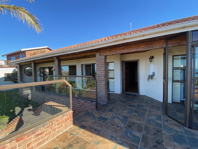 A spacious covered patio featuring slate tile flooring, brick support pillars, and a glass balustrade, offering a seamless transition to the outdoor area.