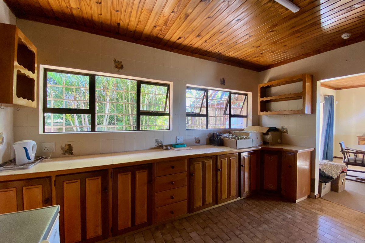 A dated kitchen featuring wooden cabinetry, tiled countertops, and a timber tongue and groove ceiling, offering significant potential for a modern renovation.