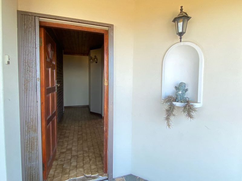 Entrance area featuring a timber door, a decorative wall niche, and an exterior wall light, leading into a tiled hallway.