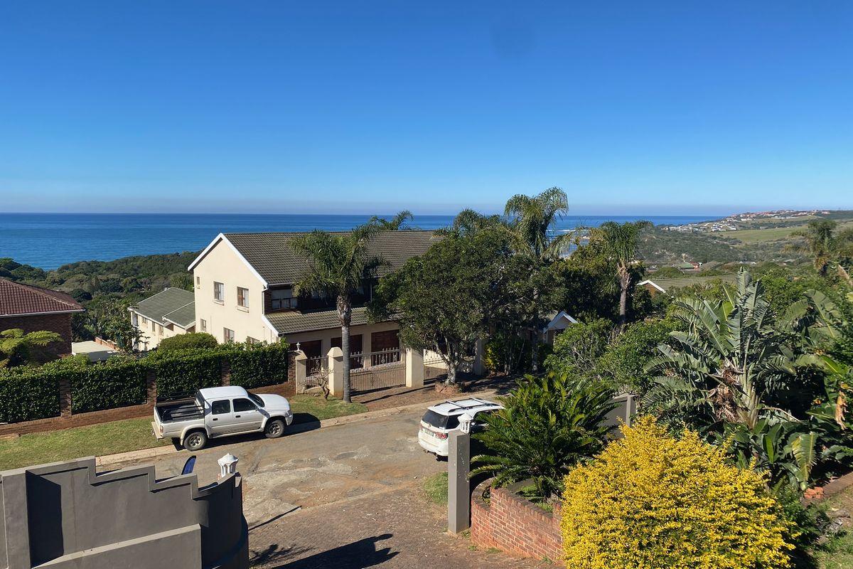 An elevated aerial view of the property showing the driveway, surrounding garden, and the coastal landscape with ocean views in the background.