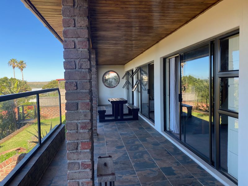 A covered patio featuring slate tile flooring, brick pillars, and a timber ceiling, offering direct access to the garden through sliding glass doors.