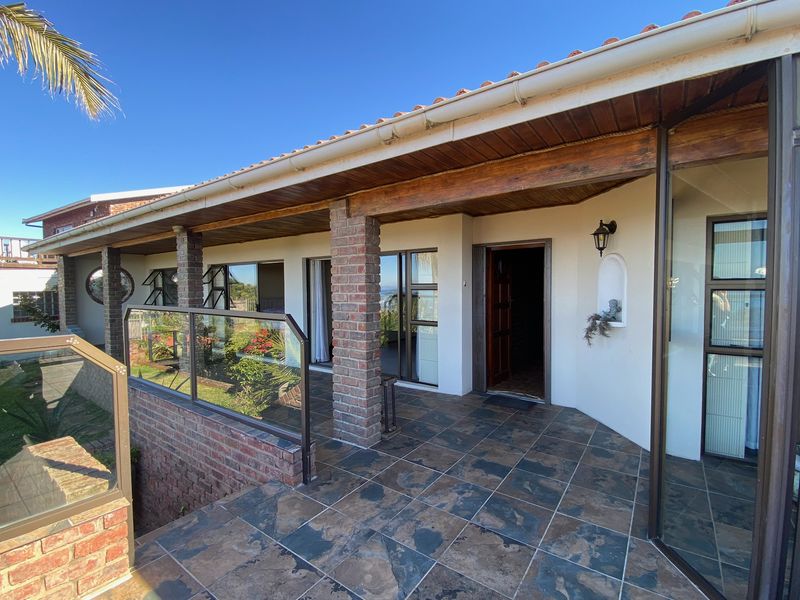 A spacious covered patio featuring tiled flooring, brick support pillars, and a glass balustrade, offering a functional outdoor living space.
