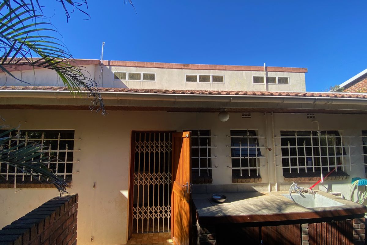 Rear exterior view of the property featuring a tiled roof, security bars on windows, a security gate, and an external utility sink area.