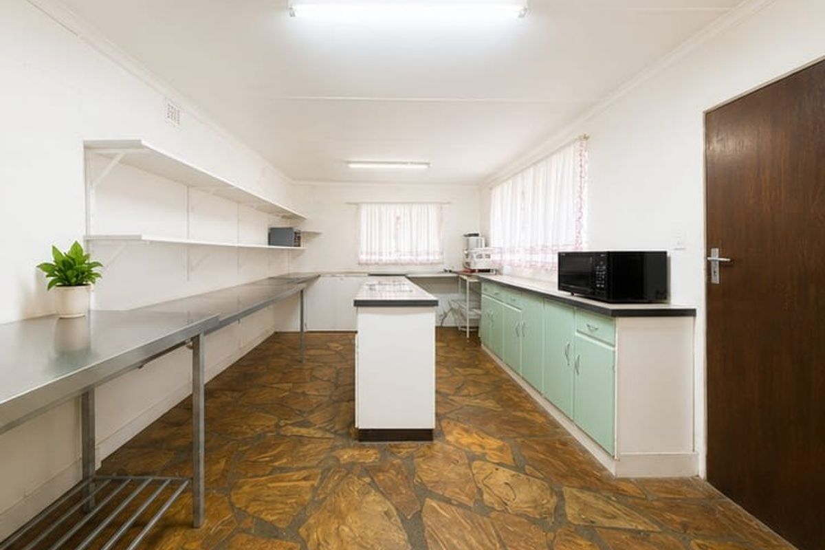 A functional commercial-style kitchen featuring stainless steel prep surfaces, built-in cabinetry, and durable stone flooring, suitable for high-volume food preparation.