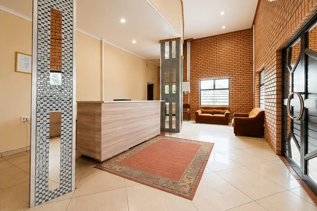 Spacious guest house reception area featuring exposed brick walls, tiled flooring, and a built-in reception desk with modern lighting.