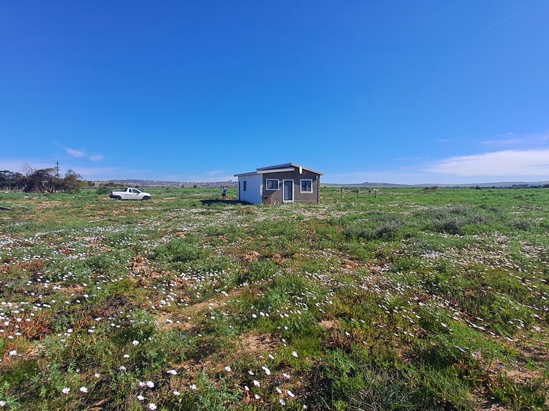 A wide-angle view of a small dwelling situated on a large, open plot of land with natural vegetation.