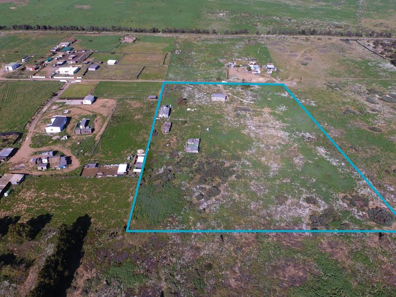 Aerial view of a large small holding property featuring expansive undeveloped land and multiple existing outbuildings within a rural setting.