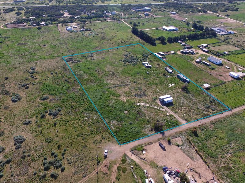 Aerial view of a large, undeveloped small holding plot with clear boundary markings, featuring natural vegetation and access to a dirt road.
