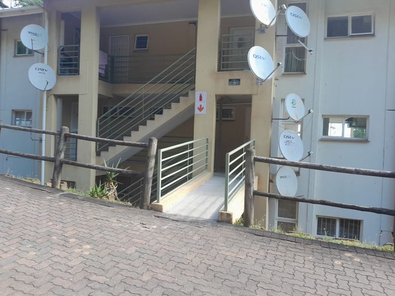 Exterior view of an apartment building entrance featuring a concrete ramp, staircase, and multiple satellite dishes mounted on the facade.
