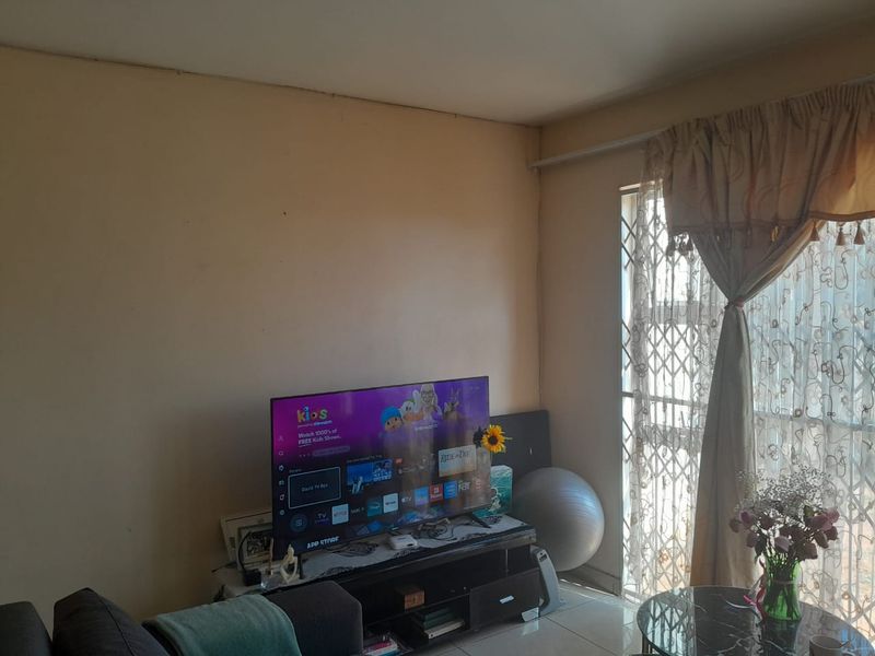 A living room area featuring tiled flooring and a security gate over the window, requiring cosmetic updates to the wall finishes.