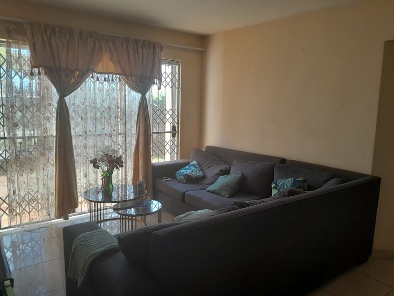 A living room featuring tiled flooring and a sliding glass door with an integrated security gate, providing access to the exterior.