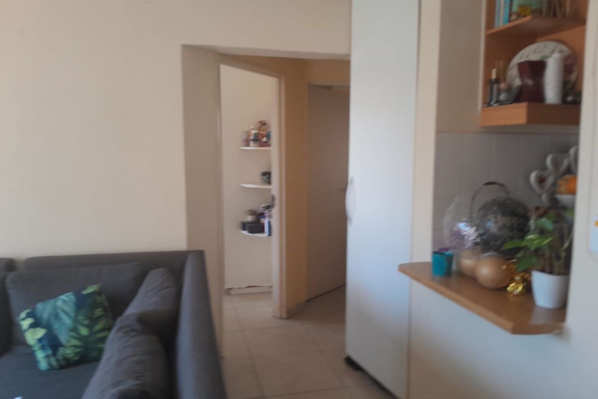 A living area featuring tiled flooring, a built-in cupboard, and integrated shelving, providing a functional layout with access to an adjacent hallway.