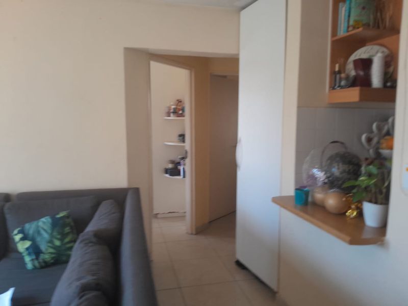 A living area featuring tiled flooring, a built-in cupboard, and integrated shelving, providing a functional layout with access to an adjacent hallway.