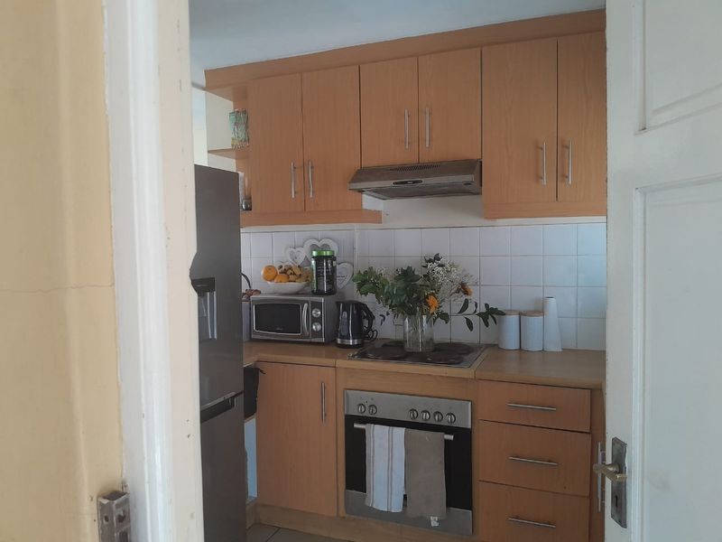 A compact kitchen featuring light wood-tone cabinetry, a tiled backsplash, and integrated cooking appliances, offering a functional layout for daily meal preparation.