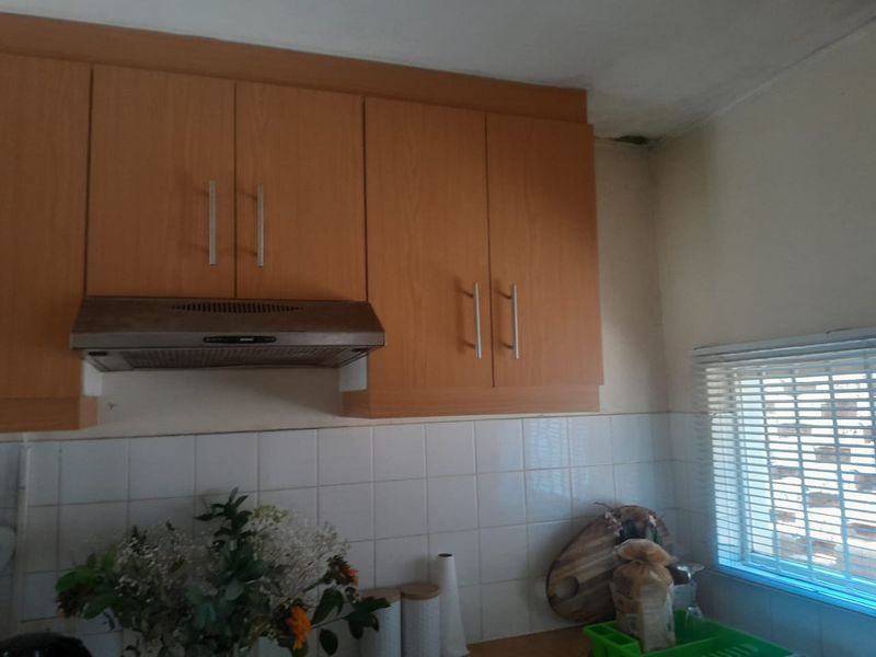 A kitchen area featuring wood-look laminate cabinetry, a built-in extractor fan, and tiled splashbacks, showing signs of ceiling water damage.
