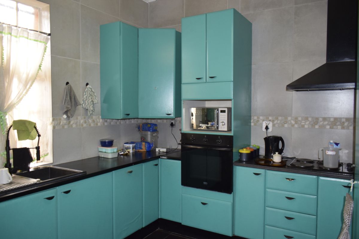 A functional kitchen featuring vibrant teal cabinetry, dark countertops, integrated oven, extractor fan, and tiled splashback with a window for natural light.