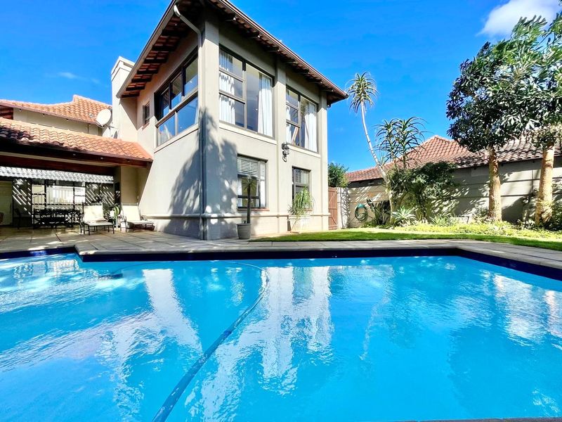 A well-maintained outdoor pool area featuring a paved patio, swimming pool, and a two-story residential structure with large windows.
