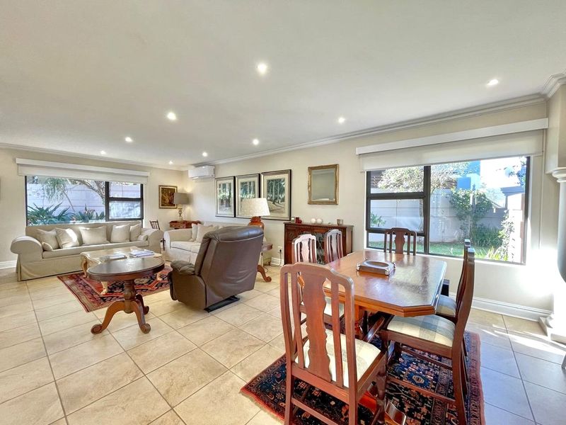 Spacious open-plan living and dining area featuring neutral tiled flooring, recessed lighting, and large windows with roller blinds, offering a bright and functional layout.