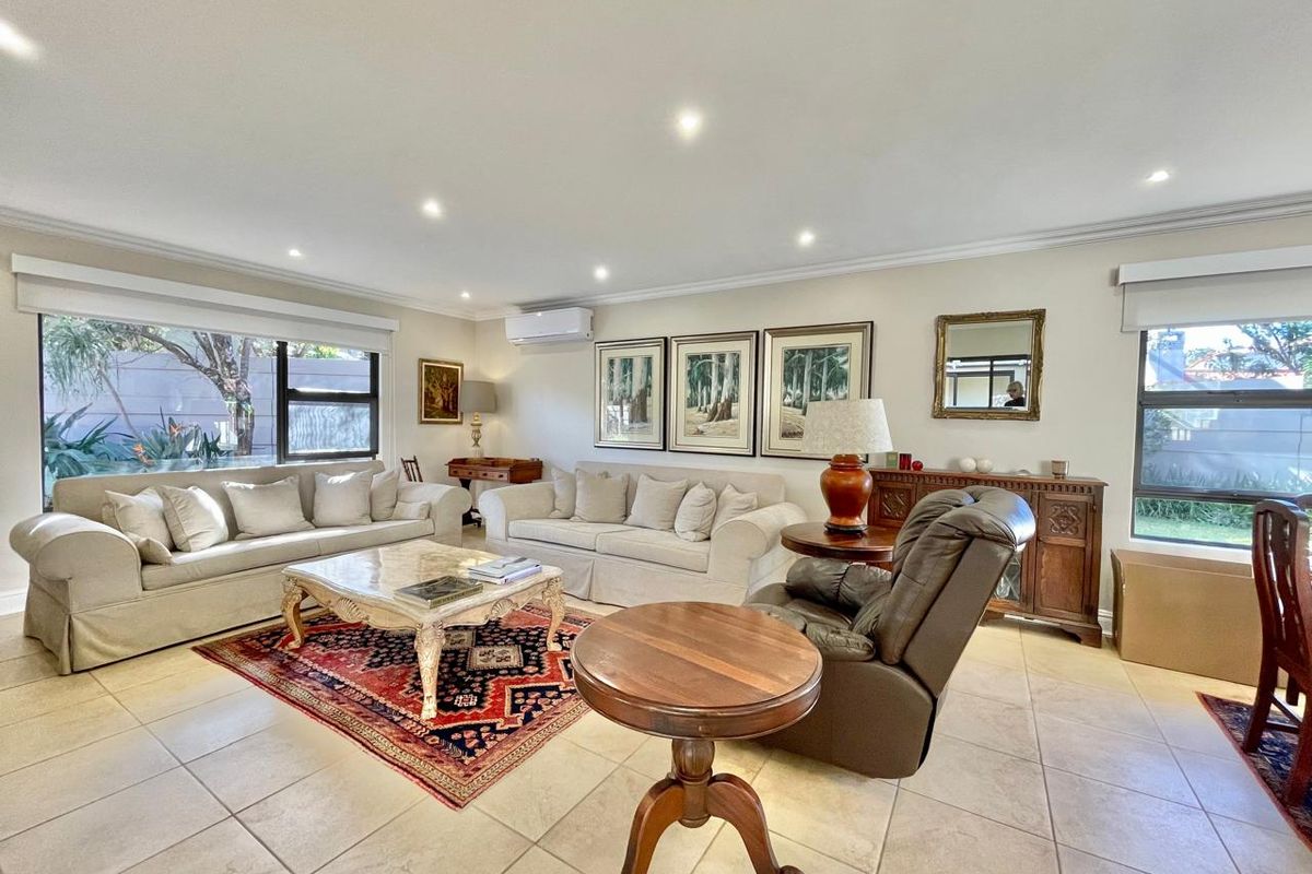 Spacious living room featuring neutral tiled flooring, recessed downlighting, and a wall-mounted split-system air conditioner, offering a bright and comfortable atmosphere.