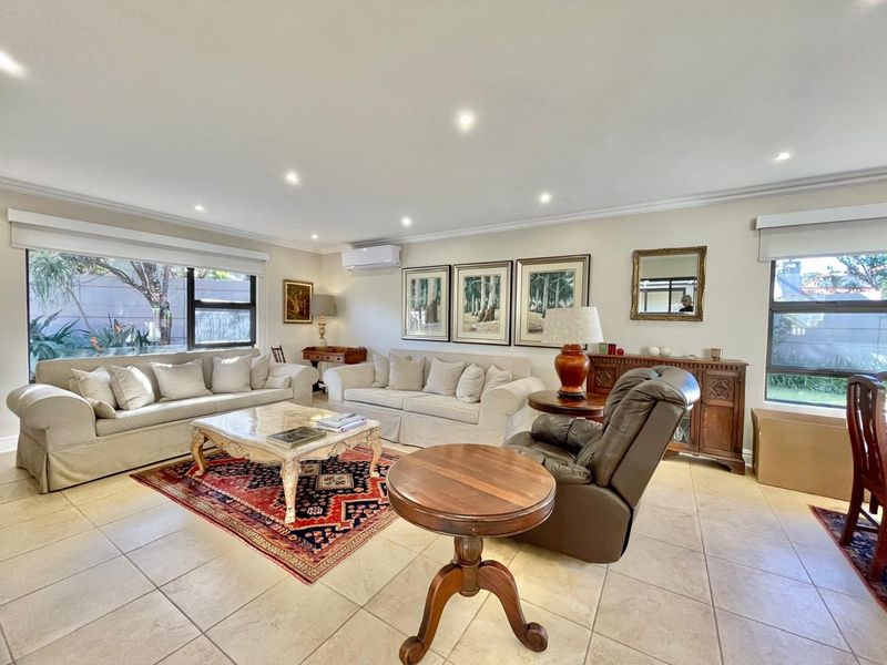 Spacious living room featuring neutral tiled flooring, recessed downlighting, and a wall-mounted split-system air conditioner, offering a bright and comfortable atmosphere.