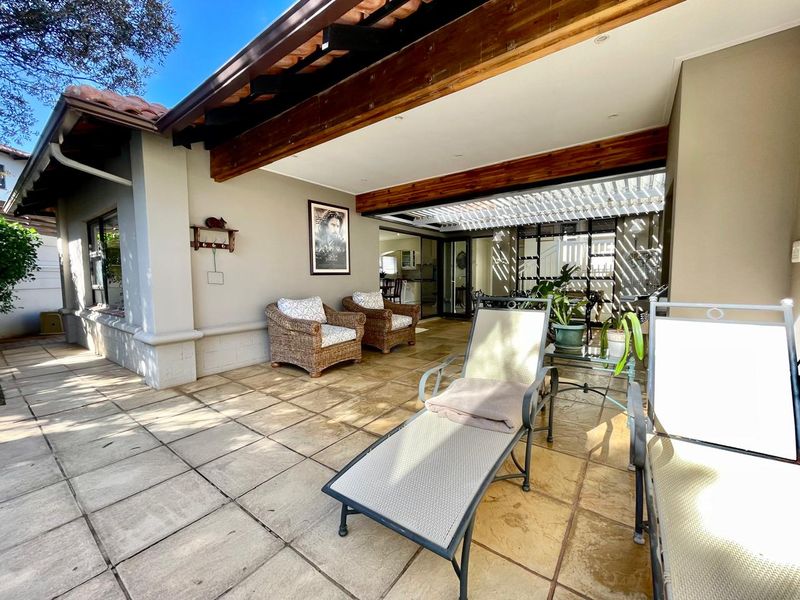 A spacious covered patio featuring tiled flooring, exposed timber beams, and a pergola, providing a seamless transition to the interior living space.