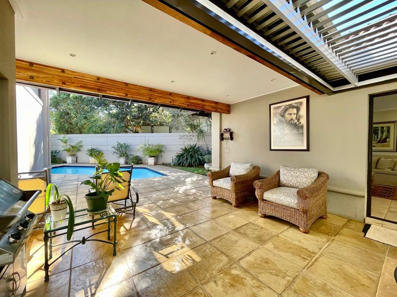 Covered outdoor patio featuring a louvered roof, tiled flooring, and recessed lighting, overlooking a private swimming pool and garden area.