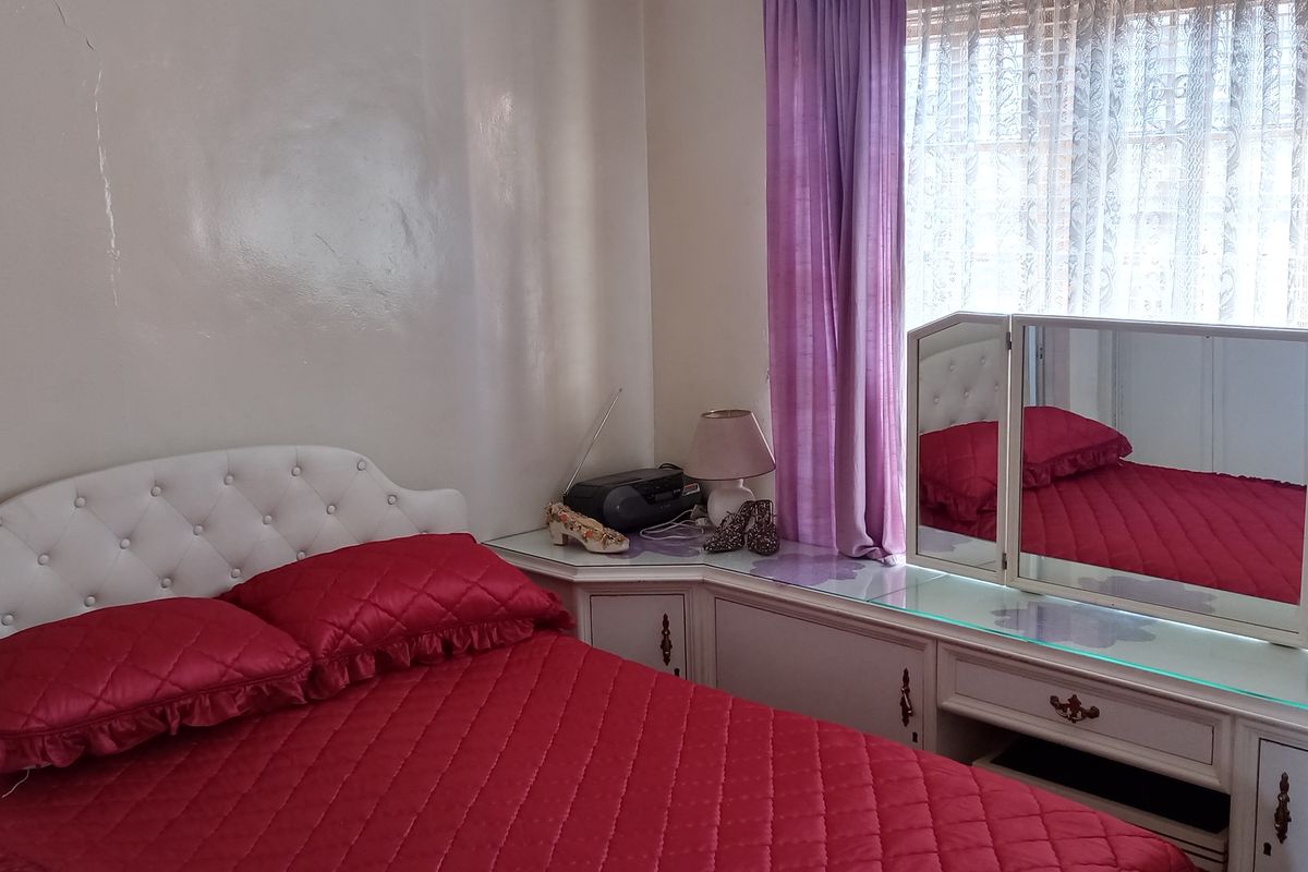 A bedroom featuring built-in cabinetry and a vanity unit, showing signs of wear including visible wall cracks.