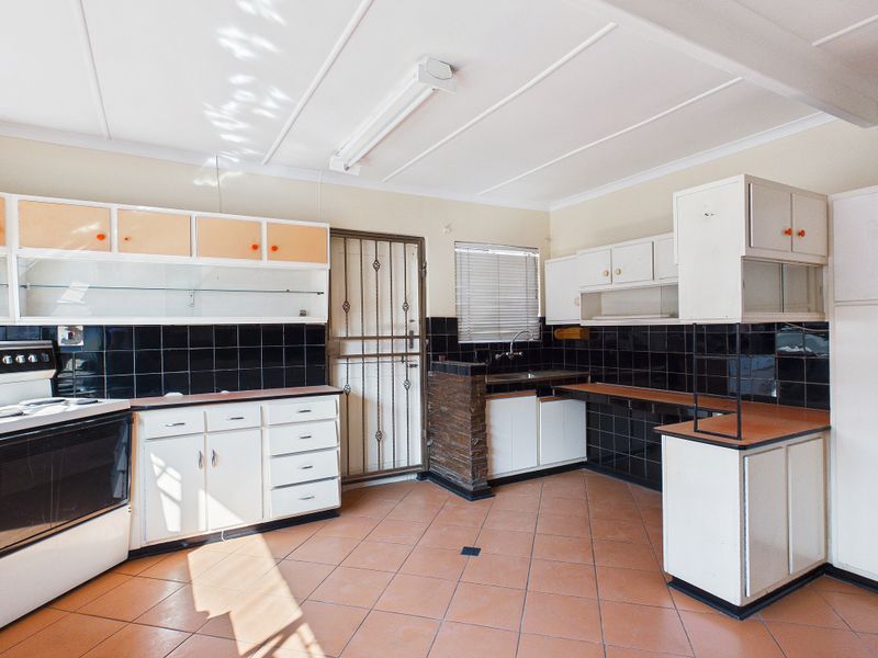 A spacious, dated kitchen featuring original cabinetry, tiled flooring, and a black tiled backsplash, offering significant potential for a modern renovation.