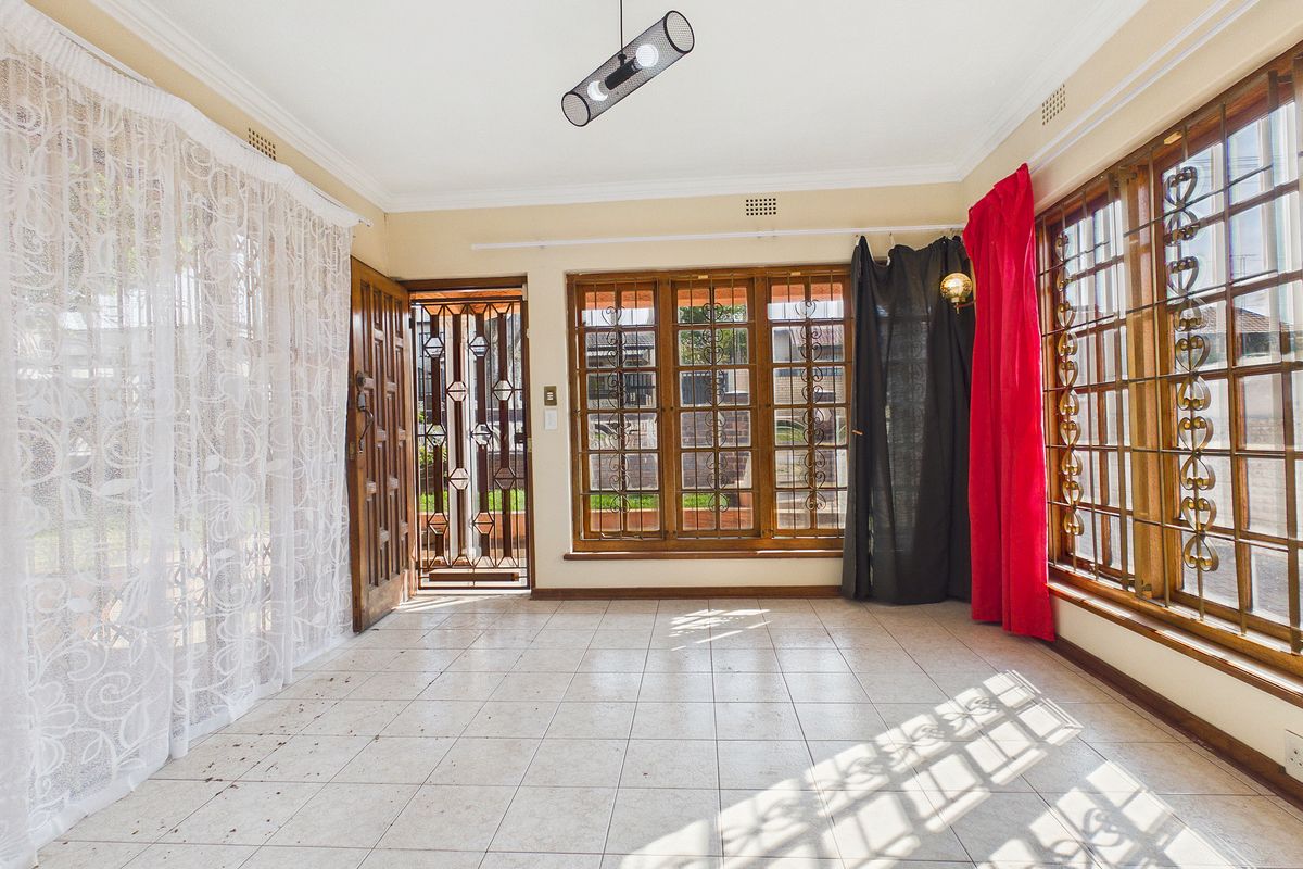 An empty living area featuring tiled flooring, wooden window frames with security bars, and a security gate leading to the exterior.