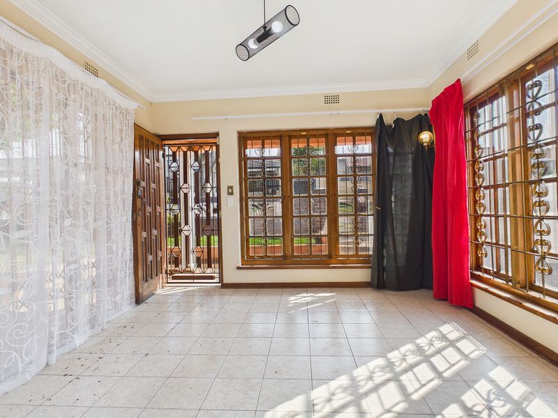 An empty living area featuring tiled flooring, wooden window frames with security bars, and a security gate leading to the exterior.