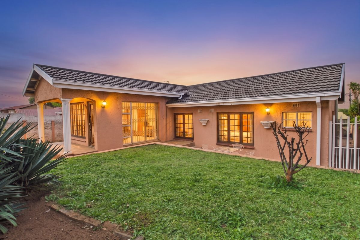 Rear view of the house featuring a covered patio, well-maintained lawn, and secure window and door fittings at dusk.