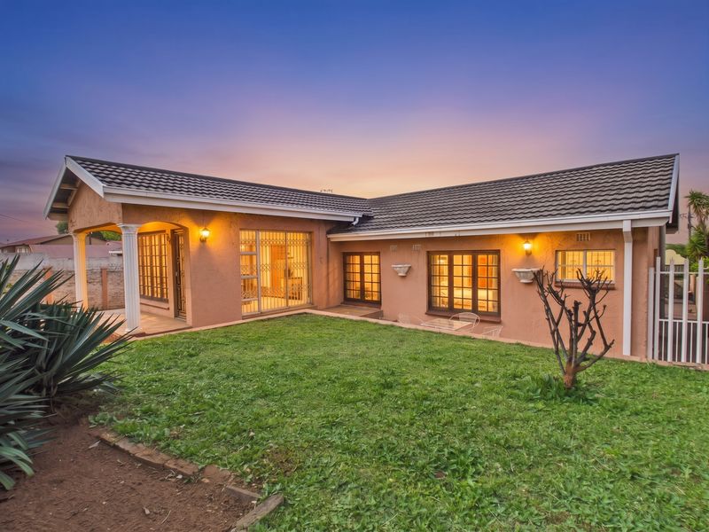 Rear view of the house featuring a covered patio, well-maintained lawn, and secure window and door fittings at dusk.