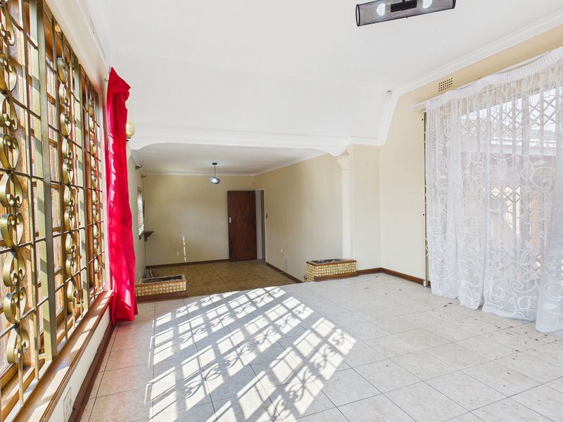 Spacious, sunlit living area featuring tiled flooring, decorative metal security grilles, and a coved ceiling, offering a blank canvas for interior design.