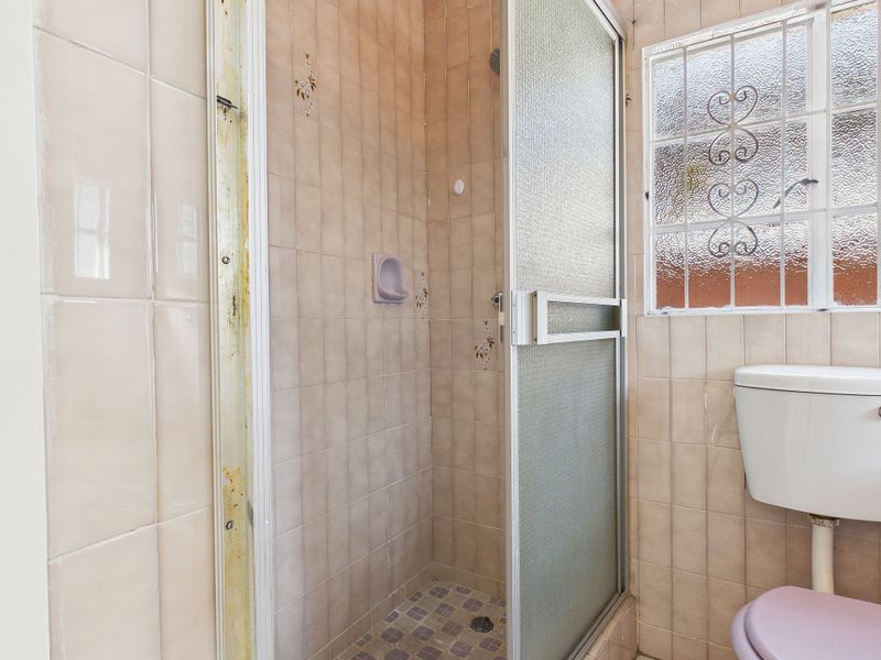 A dated bathroom featuring a shower enclosure, ceramic wall tiling, and a standard toilet, requiring modernization of finishes and fixtures.