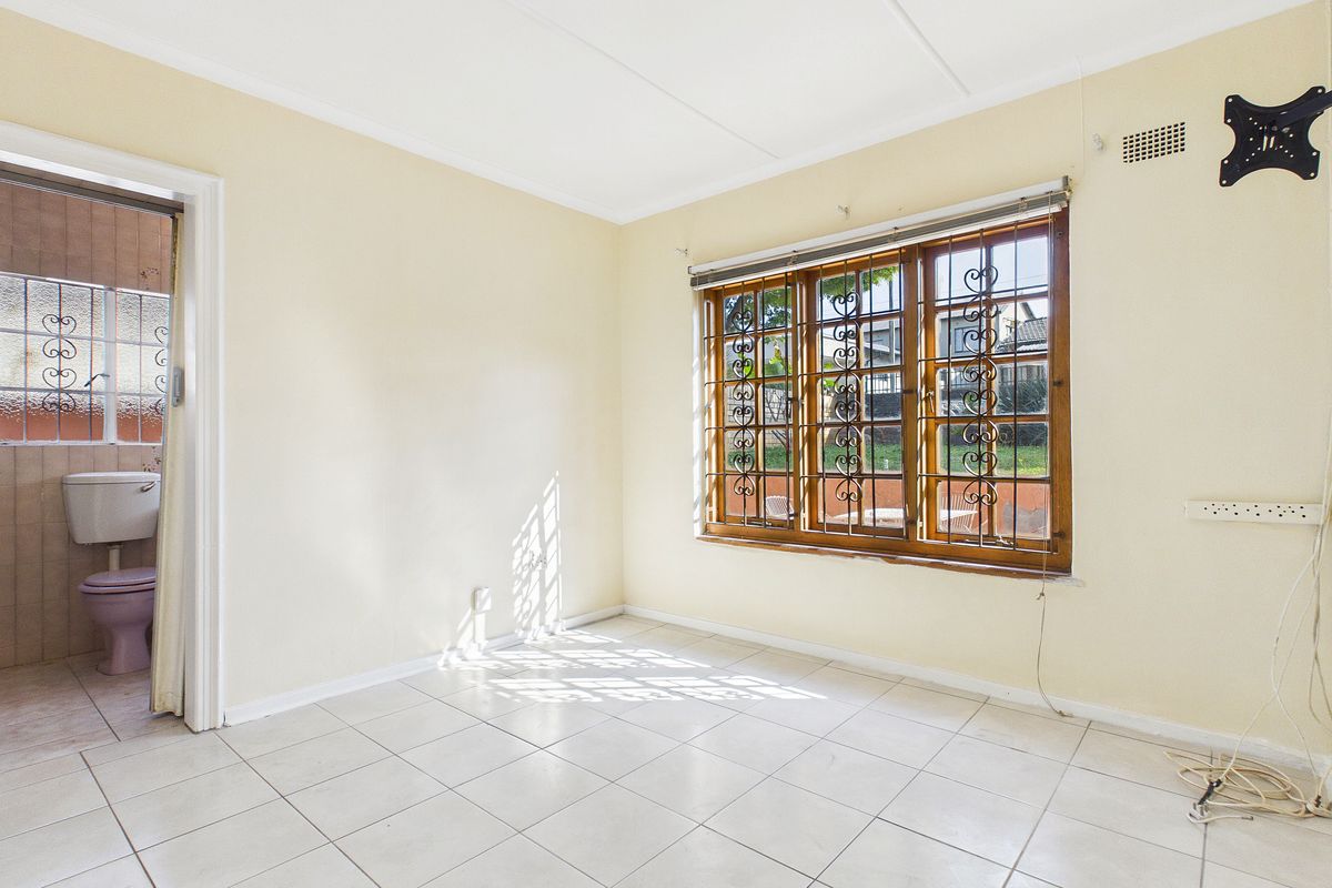 A vacant bedroom featuring tiled flooring, wooden window frames with security bars, and an adjoining bathroom.