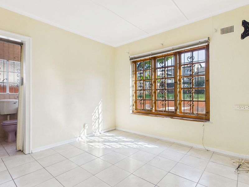 A vacant bedroom featuring tiled flooring, wooden window frames with security bars, and an adjoining bathroom.