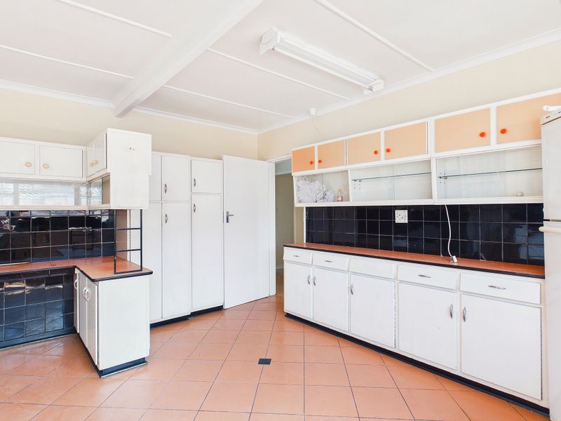 A spacious, dated kitchen featuring extensive built-in cabinetry, black tiled backsplash, and terracotta-style floor tiles, offering significant potential for a modern renovation.