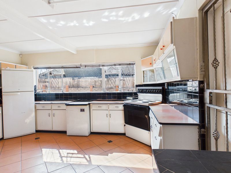 A dated kitchen featuring original cabinetry, tiled backsplash, and tiled flooring, offering significant potential for a modern renovation and layout update.