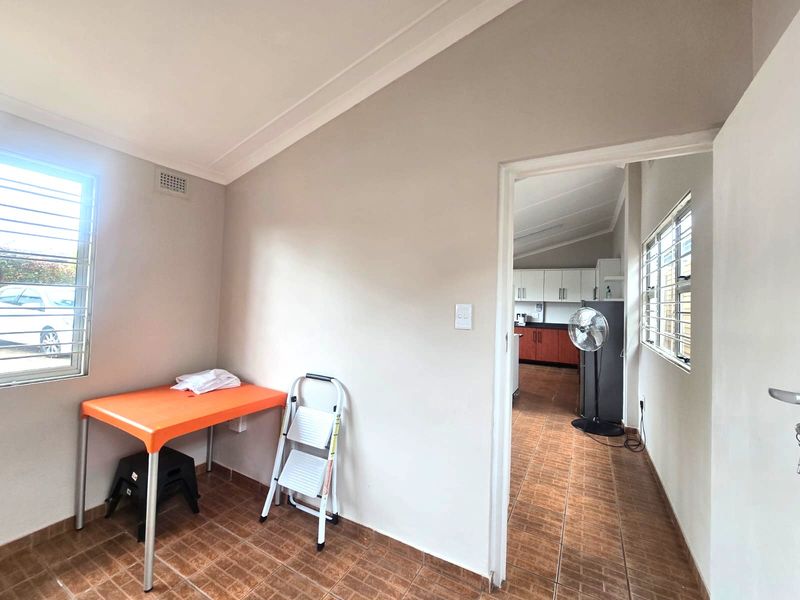 A bright, tiled living area featuring louvered windows and cove cornicing, providing a clean, neutral space with direct access to the adjoining kitchen.
