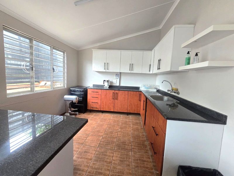 A functional kitchen featuring wood-tone and white cabinetry, granite countertops, tiled flooring, and a large window with security bars.