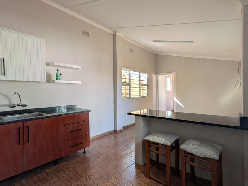Open plan kitchen featuring wooden cabinetry, granite countertops, a breakfast bar, and tiled flooring, flowing into an adjacent living area.
