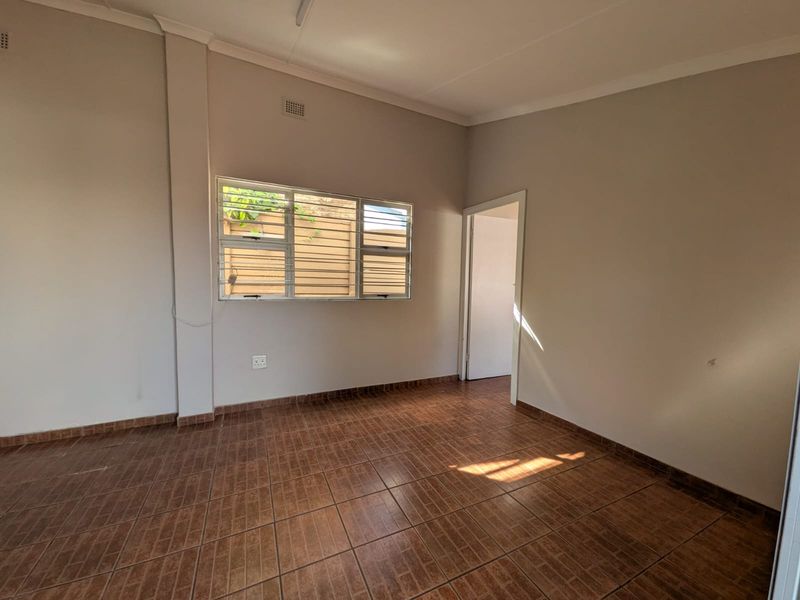 A vacant bedroom featuring tiled flooring, neutral walls, and a window fitted with security burglar bars.