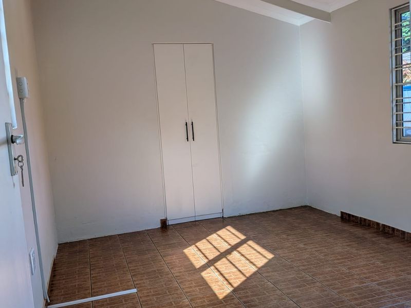A bright, empty bedroom featuring tiled flooring, a vaulted ceiling, and a built-in wardrobe, offering a clean and neutral space ready for furnishing.