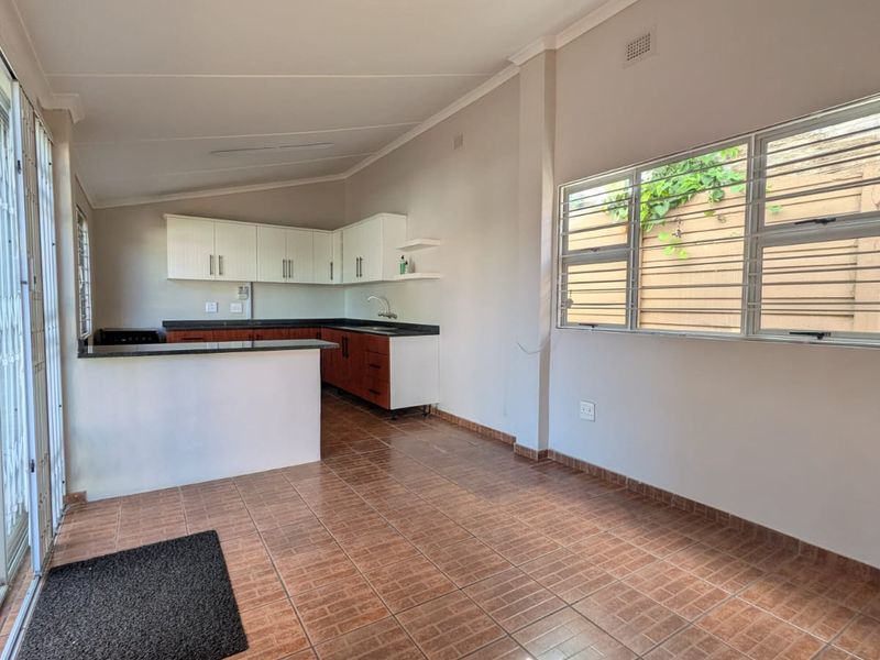 Open plan kitchen and living area featuring tiled flooring, built-in cabinetry with granite countertops, and large windows with security bars.